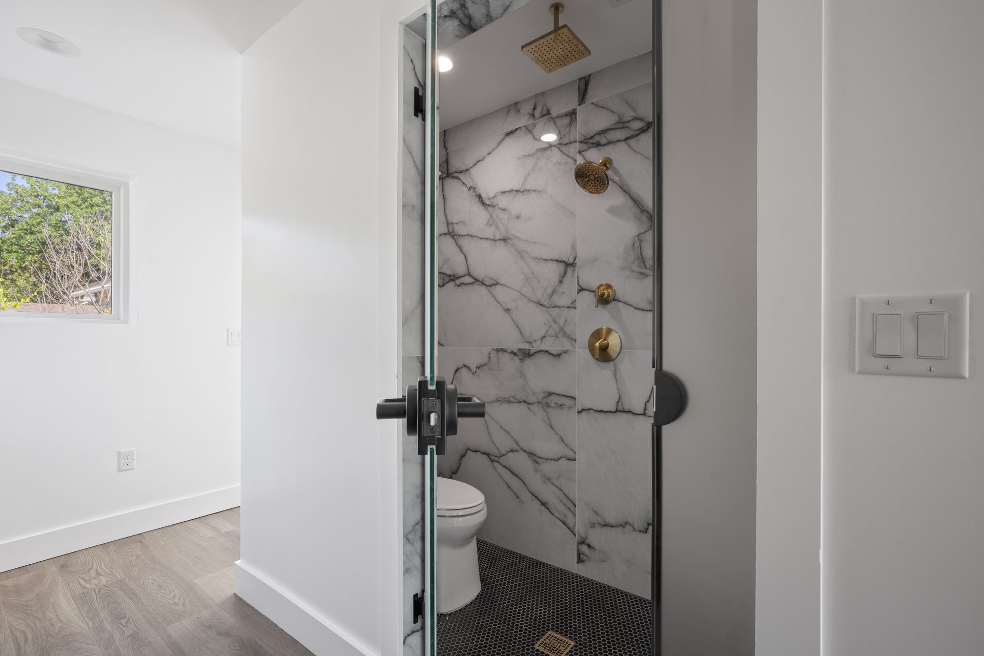Rosewood custom new build, primary bathroom shower with marble tile and brass rain head, East Austin, TX